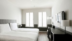 Ein Hotelzimmer mit einem großen Bett, einem Schreibtisch mit Lampe und zwei Fenstern.