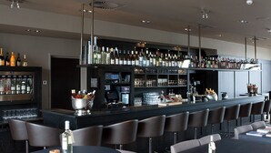Een moderne bar met een lange toonbank, diverse zitmogelijkheden en een uitgebreide selectie flessen en glazen.