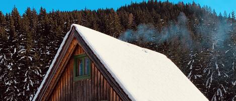 Eine Holzhütte mit schneebedecktem Dach, umgeben von verschneiter Landschaft und dichtem Wald.