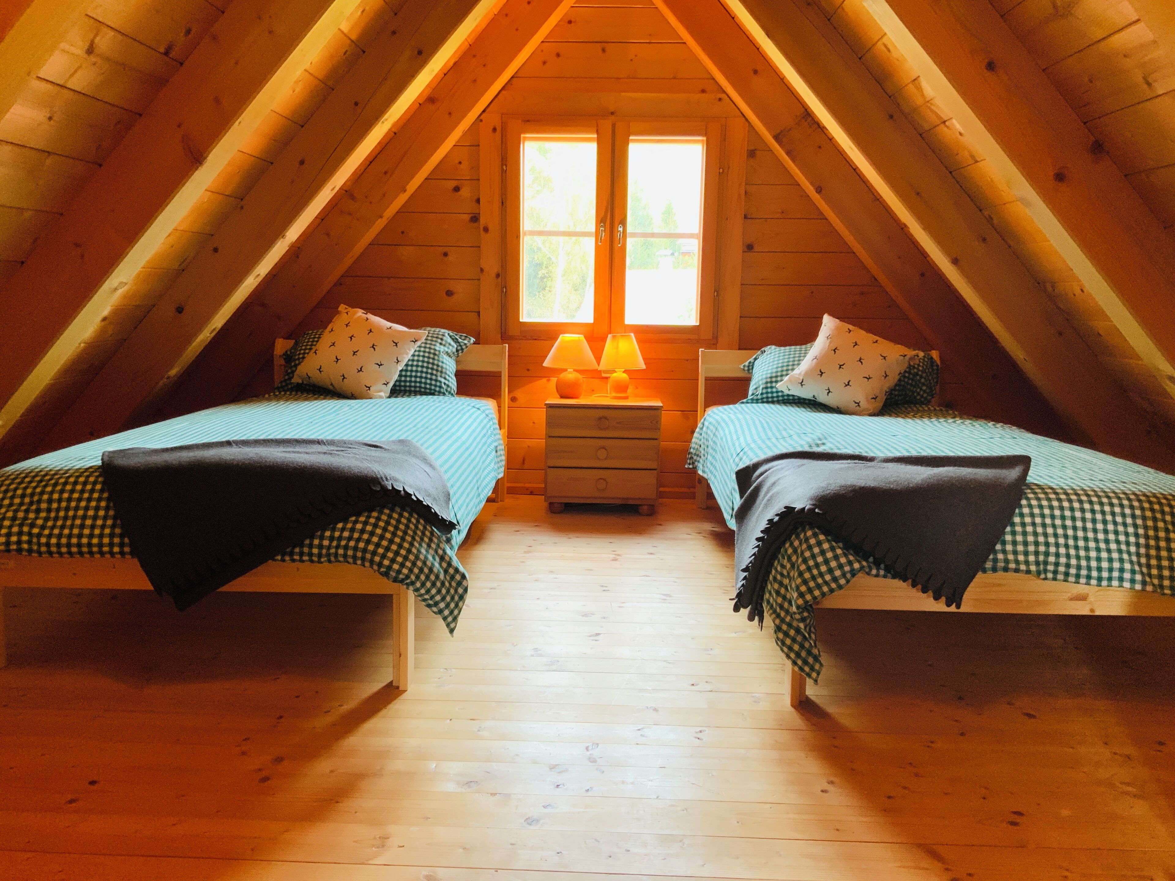 Un dormitorio acogedor en el ático con dos camas, una mesita de noche y una ventana con luz natural.