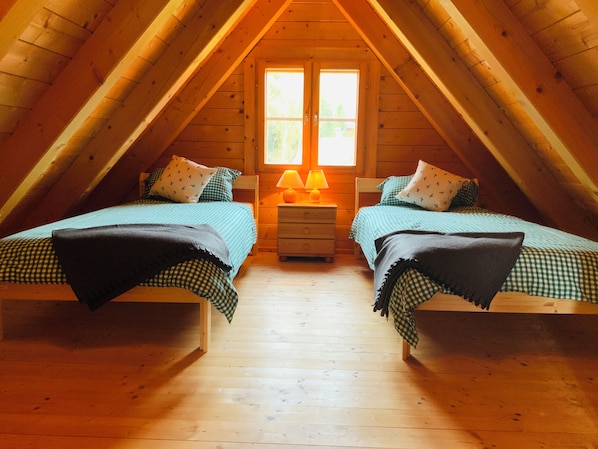 Un dormitorio acogedor en el ático con dos camas, una mesita de noche y una ventana con luz natural.