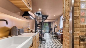 A modern kitchen with a central island, a black spiral staircase, and a stone wall. - Keepers Lodge - Sleeps 4 (Nottingham)