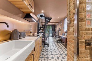 A modern kitchen with a central island, a black spiral staircase, and a stone wall. - Keepers Lodge - Sleeps 4 (Nottingham)