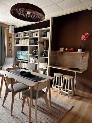Un salon moderne comprenant un coin repas, des étagères, un téléviseur et un comptoir de cuisine.