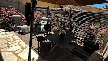 En udendørs terrasse med bord og stole, en pergola og et træhegn.