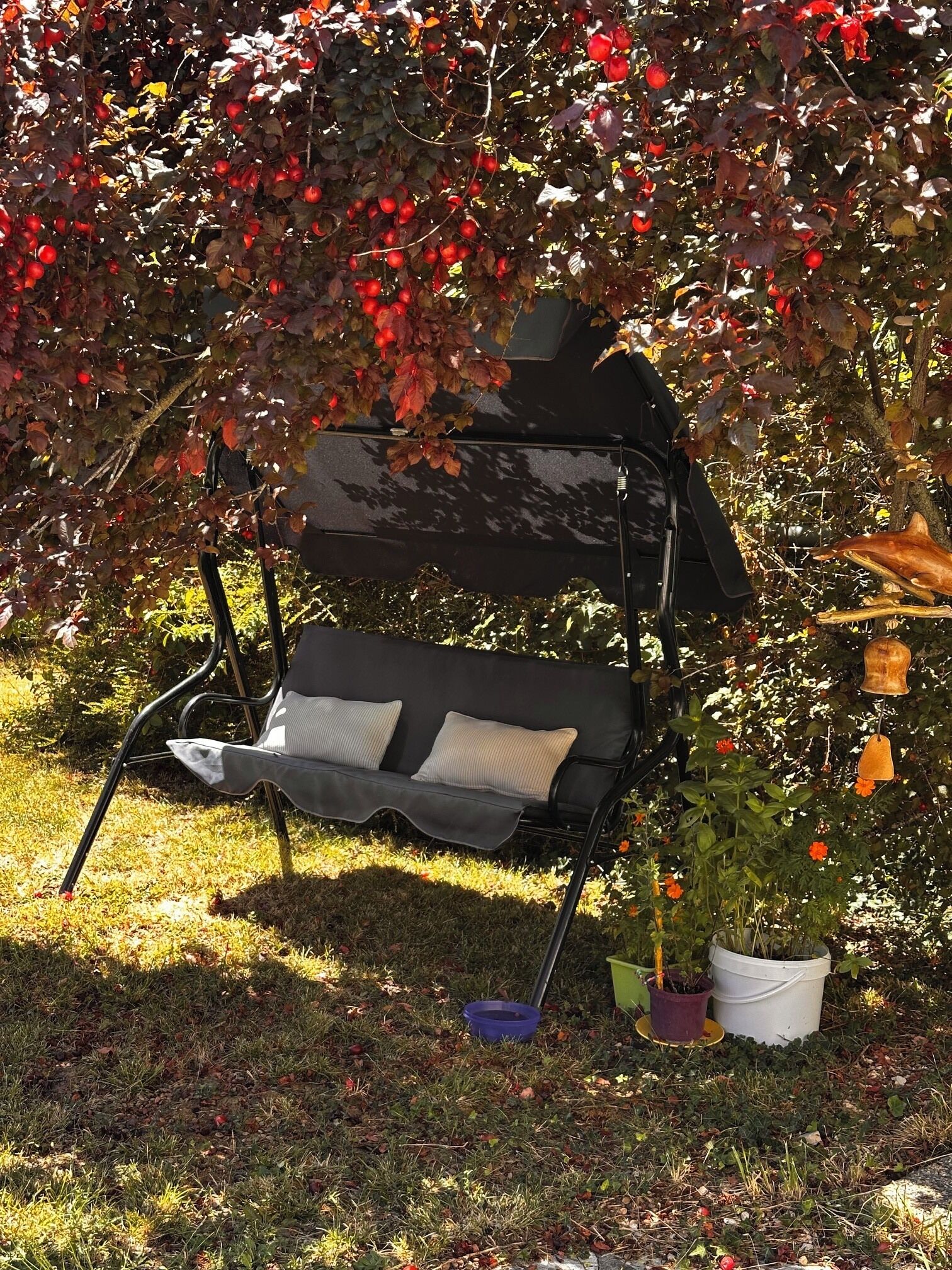 Ein schwarzer Gartenstuhl mit Kissen, ein Blumentopf und eine Metallskulptur in einem Garten.