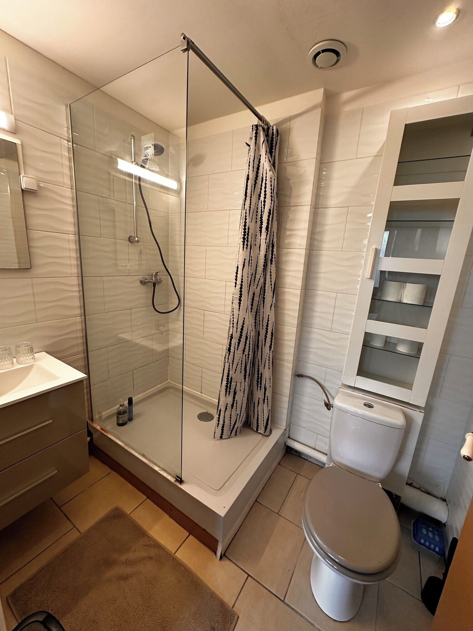 Een moderne badkamer met een douchecabine van glas, een toilet en een plank met toiletartikelen.