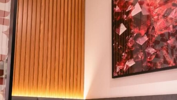Ein Hotelzimmer mit einem Bett, einem Kopfteil, einem an der Wand befestigten abstrakten Gemälde und einer Wandgestaltung aus Holzleisten.