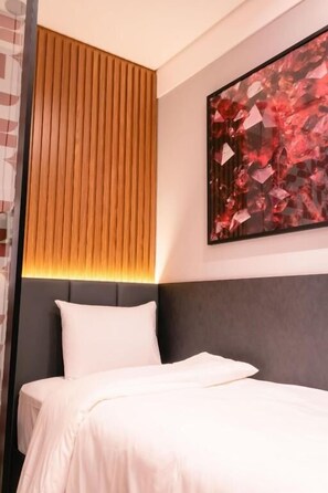 A hotel room with a bed, a headboard, a wall-mounted abstract painting, and a wooden slat design on the wall.