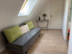 A room with a grey sofa, a small table with a lamp, and a door.