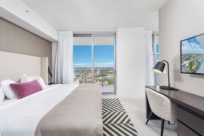 Una habitación de hotel con cama, escritorio, silla y vistas a la ciudad, además de un ventanal grande.