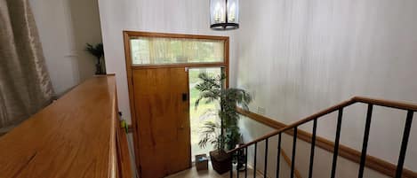 A wooden staircase with a handrail, a door with a frosted glass panel, and a hanging light fixture.