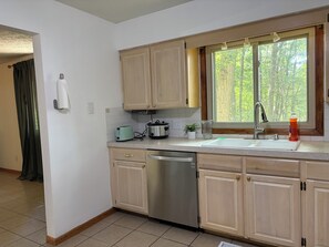 A modern kitchen with a dishwasher, a toaster, and a window with a view of trees. - The Woodlands Charity  -Large Private Room & bath in Tallmadge (Tallmadge)