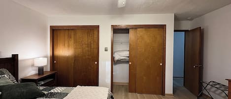 A bedroom with a bed, bedside table, lamp, wooden wardrobe, and a ceiling fan.