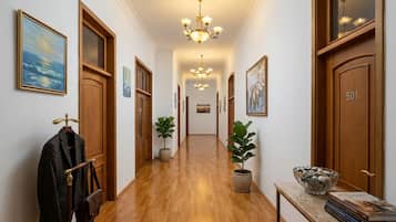 A hallway with wooden doors, a coat rack, potted plants, and a chandelier.