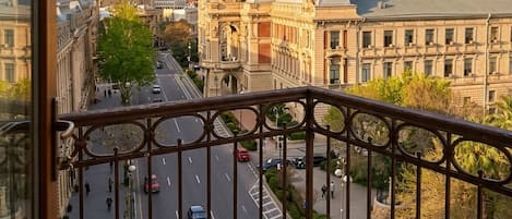 A balcony with a table set for tea, overlooking a city street with buildings and a flag.