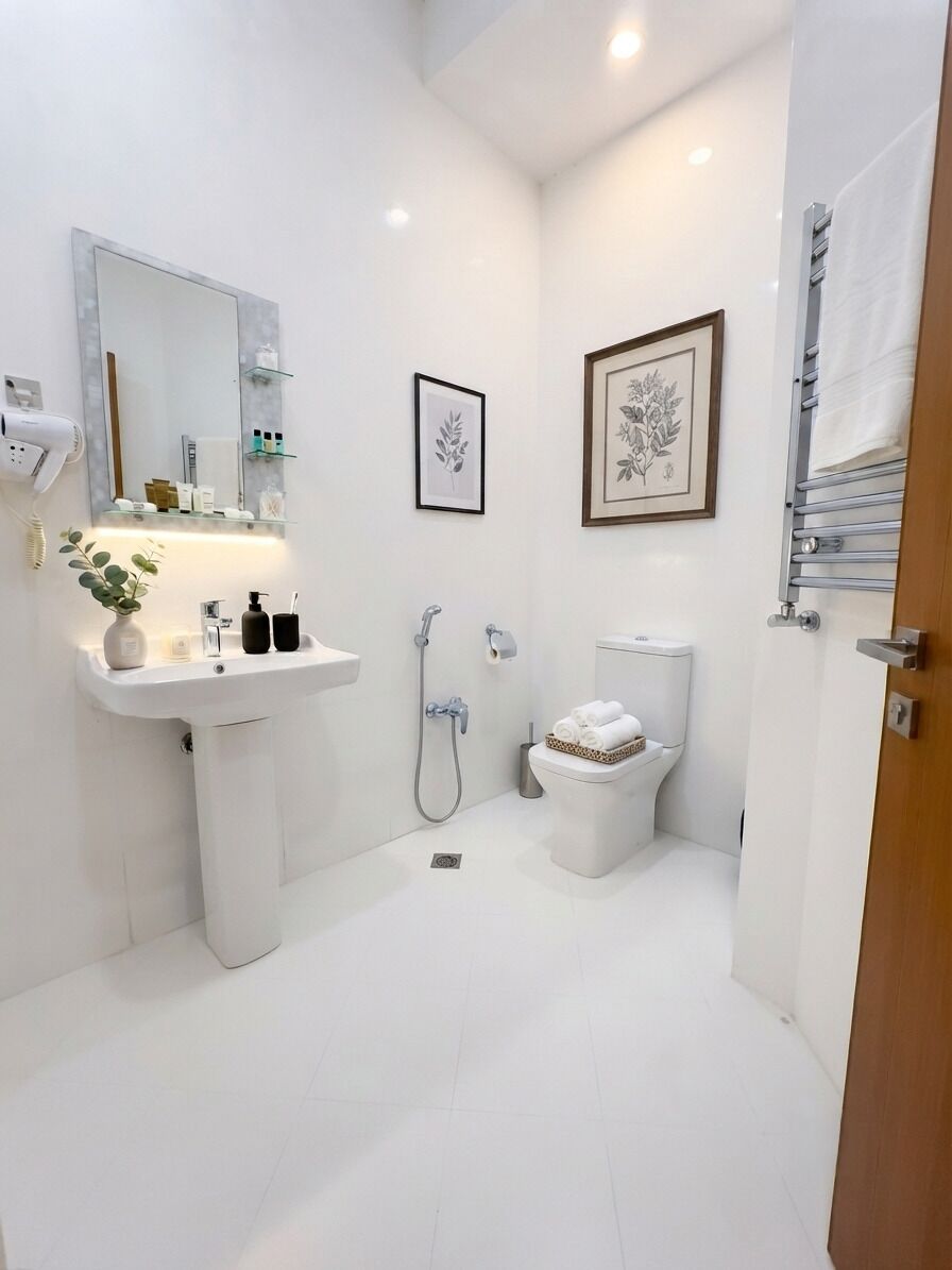 A modern bathroom with a white sink, toilet, and shower. There are framed pictures on the wall and a towel rack.