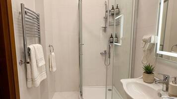 A modern bathroom with a glass-enclosed shower, a white sink with a mirror, and a towel rack with towels.