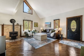 A cozy living room with a fireplace, comfortable seating, and a large window. - Forest Road Haven: 3 King BR-GameRoom-HotTub-Sauna (Rapid City)