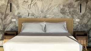 Una cama con cabecera, dos mesitas de noche y un mural de follaje en la pared.