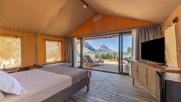 A tented room with a bed, a TV, and a view of mountains.
