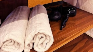 Una estante de madera con un lavabo blanco, dos botellas y toallas enrolladas.