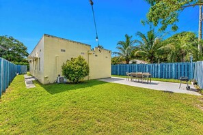 Un patio trasero cercado con un edificio, un árbol pequeño y una mesa con sillas.