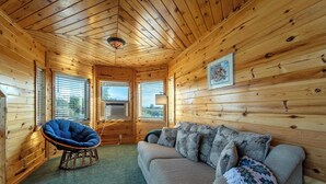 Ein gemütliches Blockhaus-Interieur mit Holzwänden, einem blauen Sessel, einem grauen Sofa und einem gerahmten Bild an der Wand.