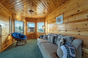 A cozy cabin interior with wooden walls, a blue chair, a grey sofa, and a framed picture on the wall. - Teton Homestead: Bear Creek Cabin Retreat (Driggs)