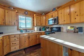A kitchen with wooden cabinets, a stainless steel microwave, and a stove. - Teton Homestead: Bear Creek Cabin Retreat (Driggs)