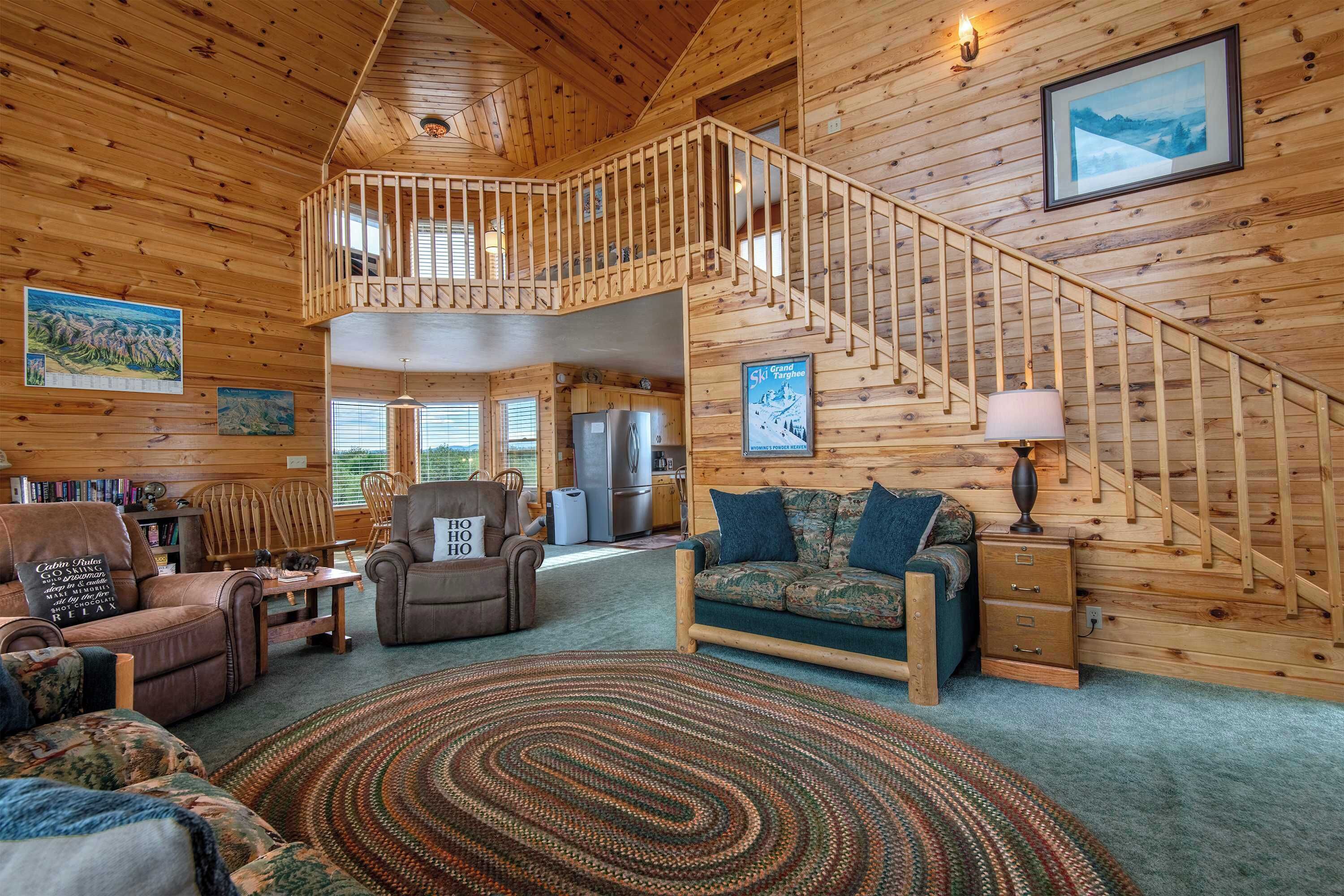 A spacious cabin interior with a wooden staircase, a cozy seating area, and a dining space.