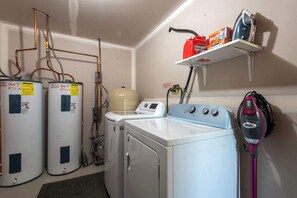 A laundry room with two water heaters, a washing machine, a dryer, and a vacuum cleaner. - Teton Homestead: Bear Creek Cabin Retreat (Driggs)
