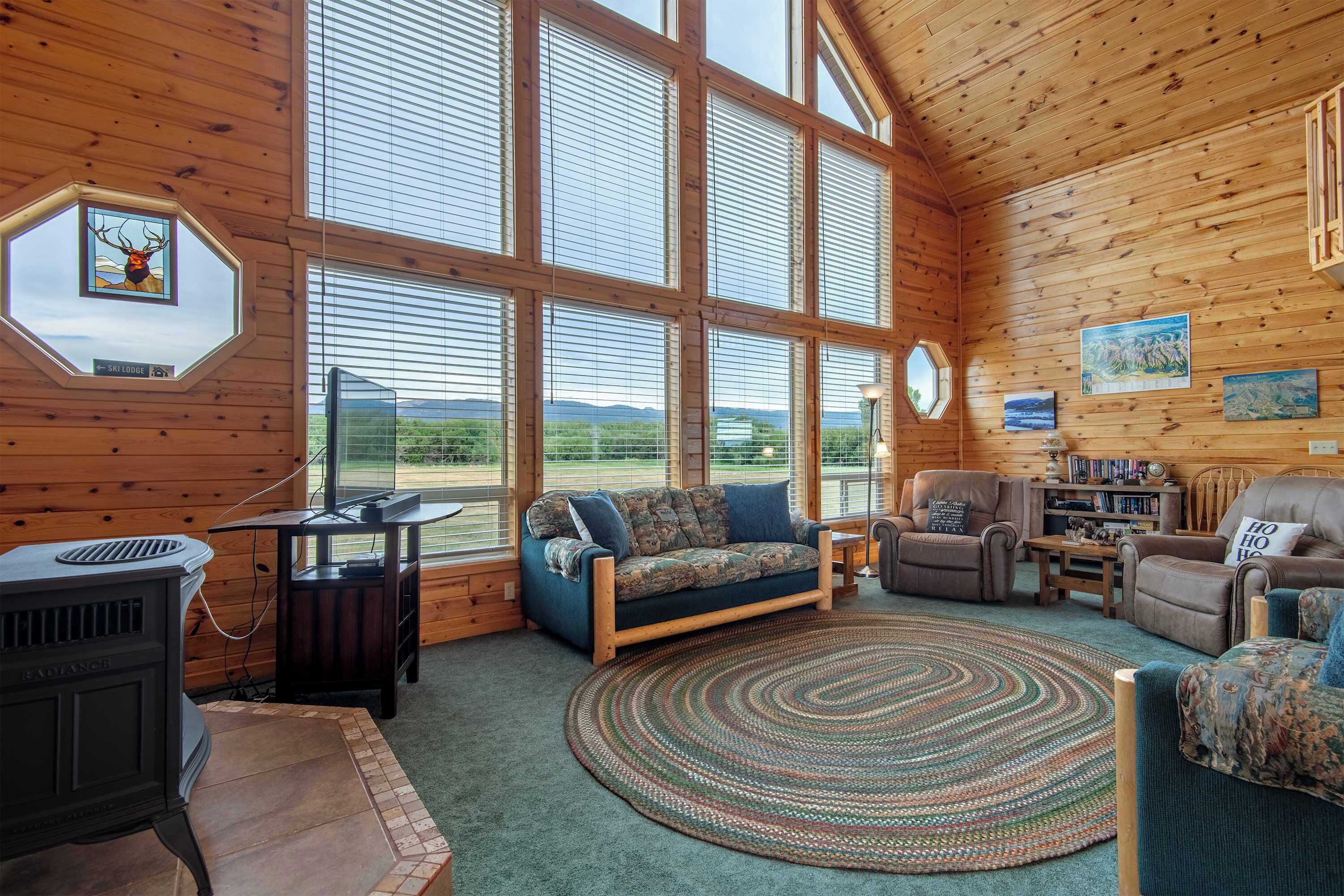 L’intérieur d’un chalet accueillant, avec une grande fenêtre, une cheminée, un canapé et un tapis.
