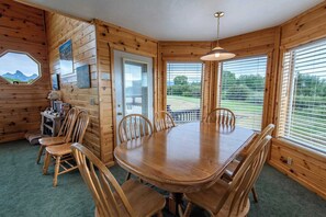 A wooden dining room with a table and chairs, a window with blinds, and a door. - Teton Homestead: Bear Creek Cabin Retreat (Driggs)