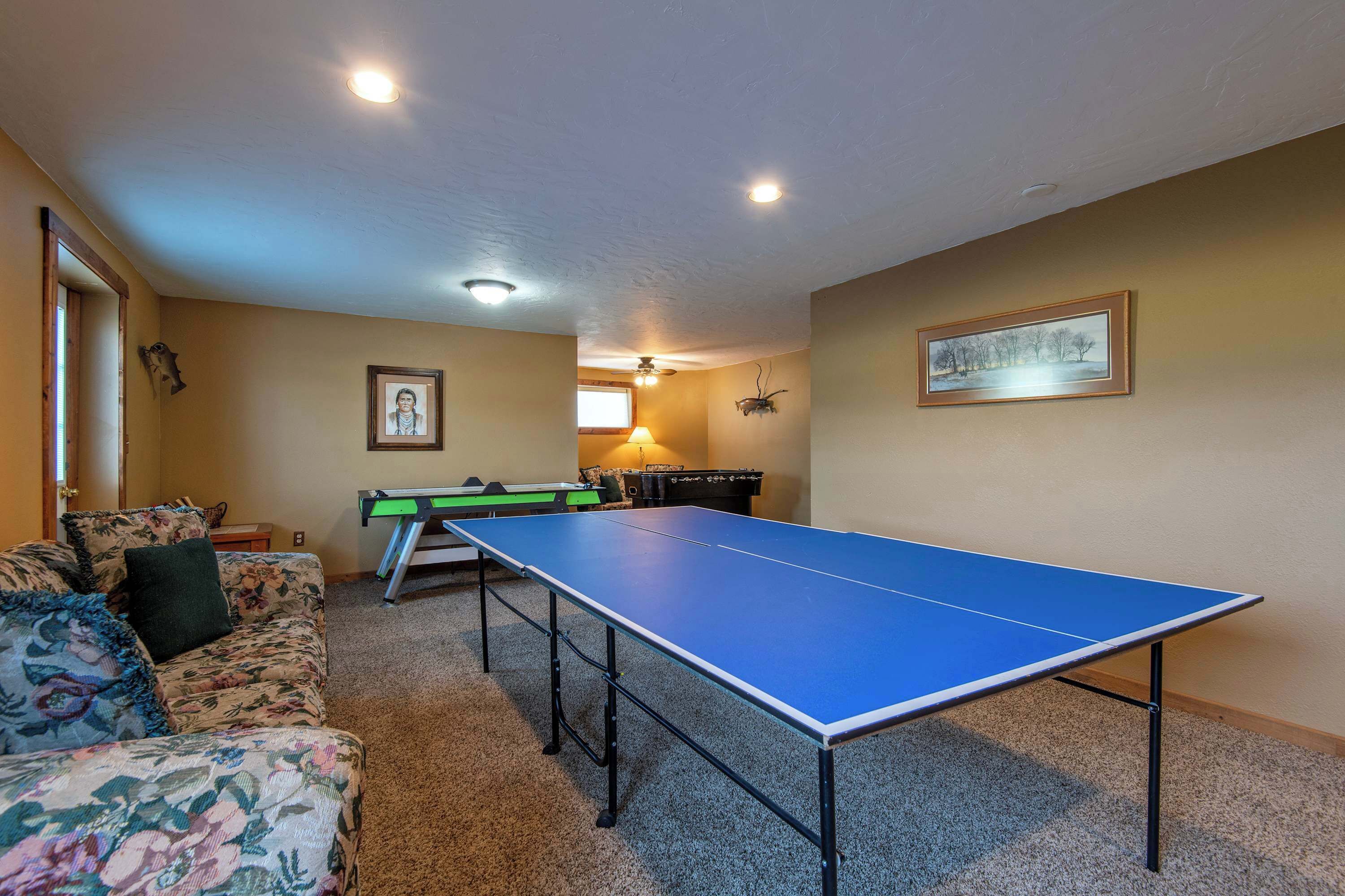Una habitación con mesa de ping pong, sofá, lámpara y un cuadro en la pared.
