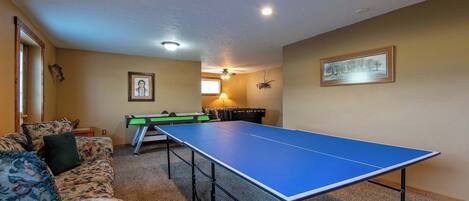 Una habitación con mesa de ping pong, sofá, lámpara y un cuadro en la pared.
