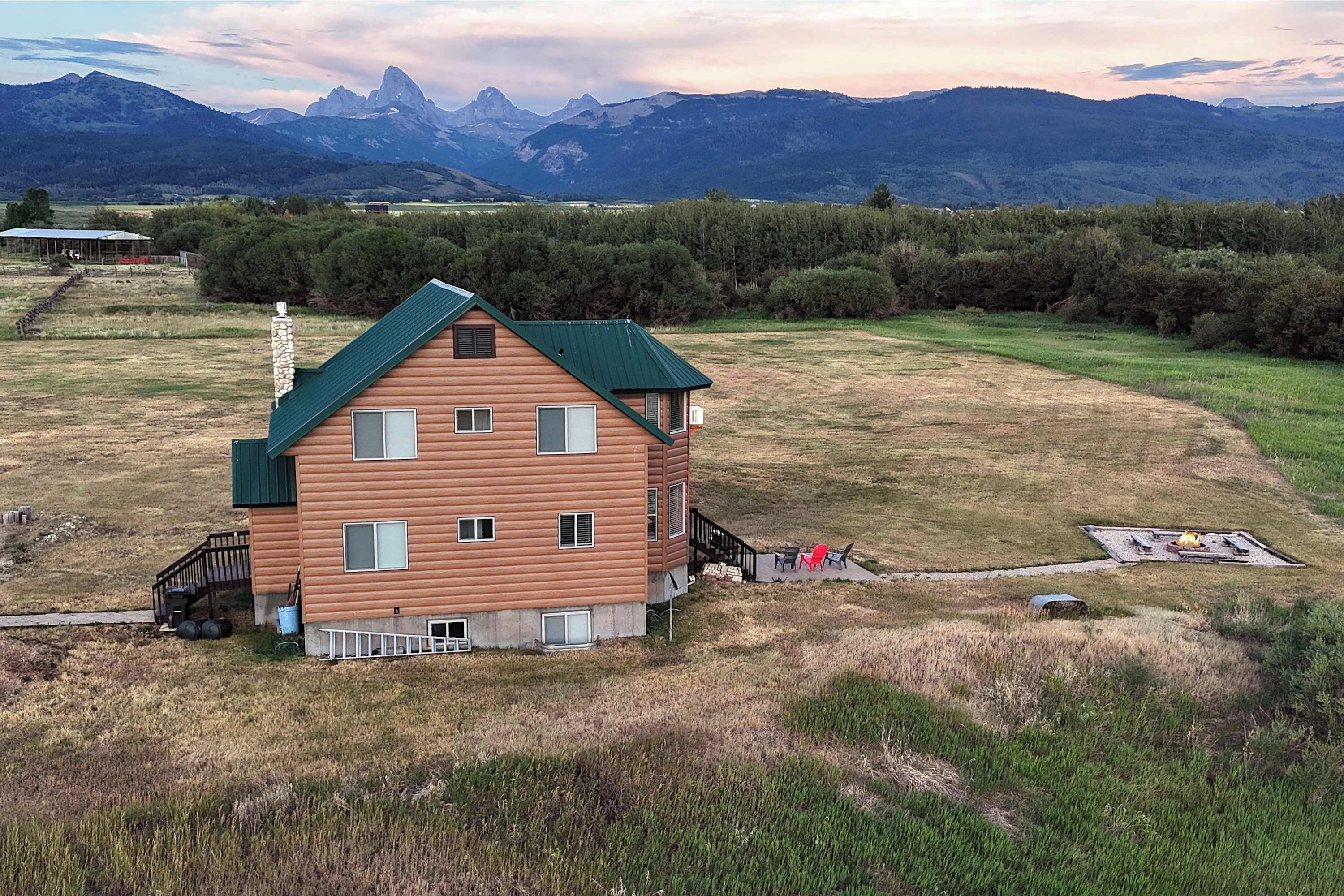 Eine zweistöckige Holzblockhütte mit grünem Dach, einer kleinen Veranda und einem Feuerstellenbereich.