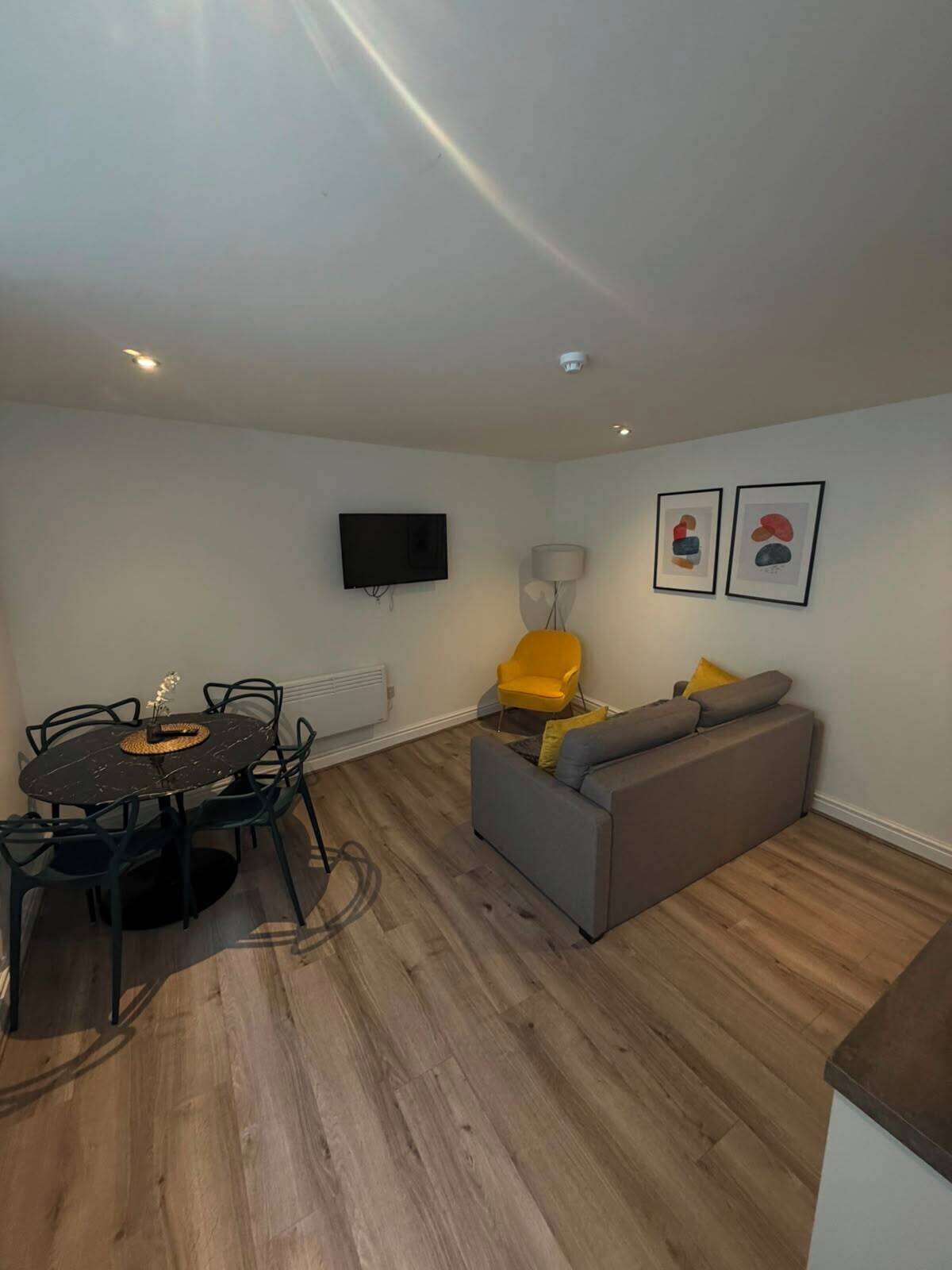 A modern living space with a dining area, a sofa, a TV, and artwork on the wall.