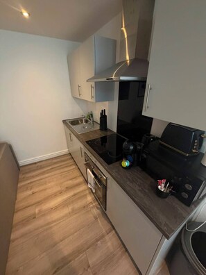 A compact kitchen with a built-in oven, a stovetop, and a sink. - Modern City Centre 1 Bedroom Apartment (Liverpool)