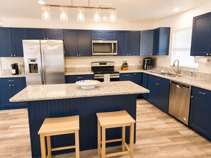A modern kitchen with dark blue cabinets, stainless steel appliances, a granite countertop, and wooden stools.