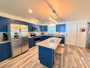 A modern kitchen with blue cabinets, stainless steel appliances, a granite countertop, and a central island.