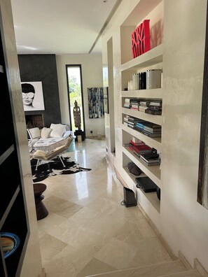 A modern living room with a white sofa, a black and white rug, and a bookshelf filled with books and decorative items. - "Le Chameau Bleu" Villa: Wellness & Luxury on a 1.5-hectare private estate (Marrakech)