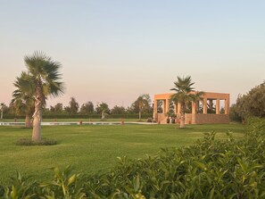 A modern outdoor pavilion with a stone facade, surrounded by a well-maintained lawn and palm trees. - "Le Chameau Bleu" Villa: Wellness & Luxury on a 1.5-hectare private estate (Marrakech)
