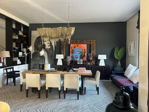 Una sala de estar moderna con comedor, que incluye una araña, obras de arte y un tapete estampado.