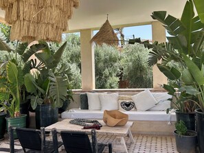 Un espacio al aire libre con luz de sol, con un sofá, sillas y plantas en macetas.