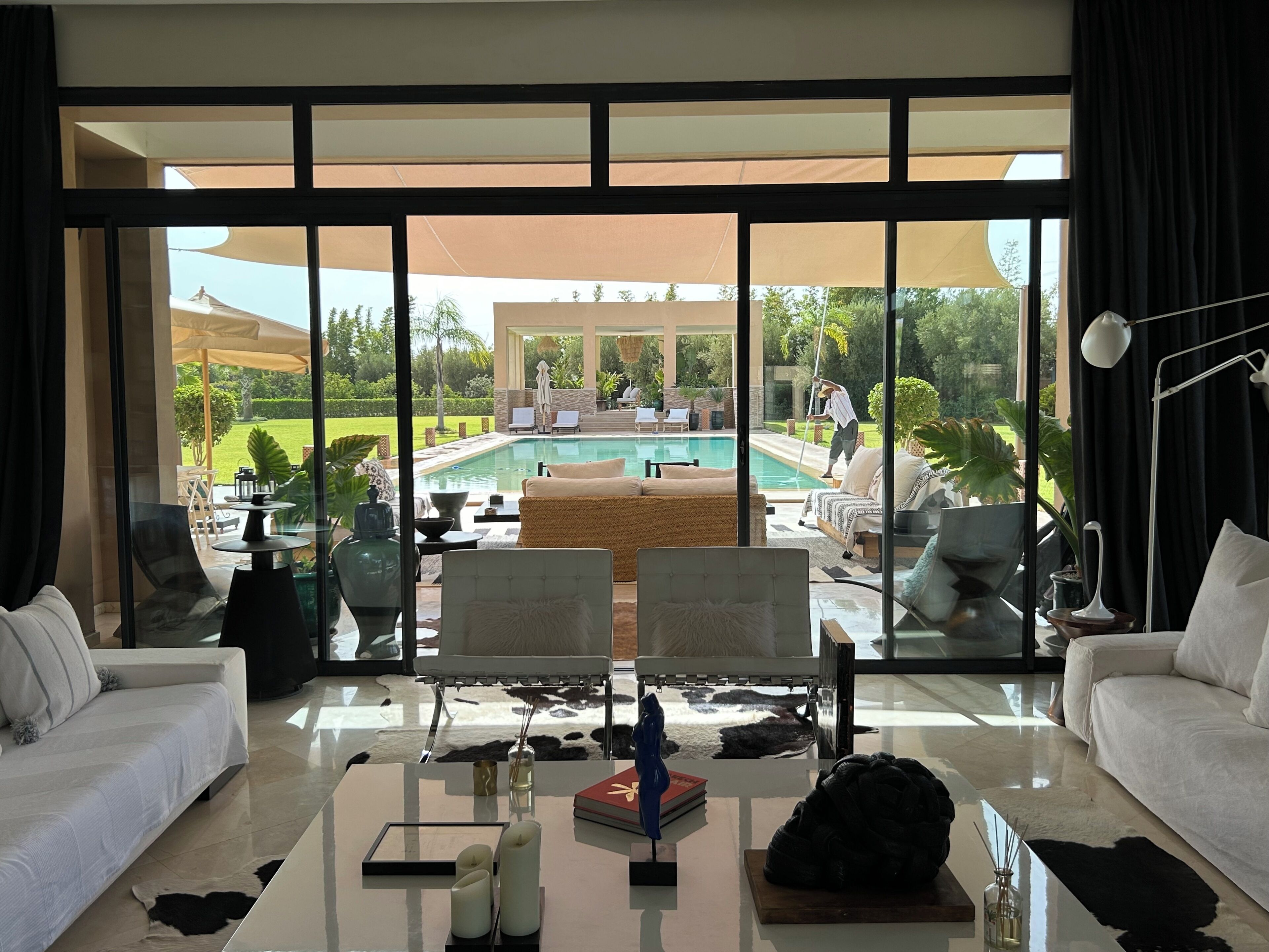 A spacious living area with a large glass wall, a pool, and outdoor seating.