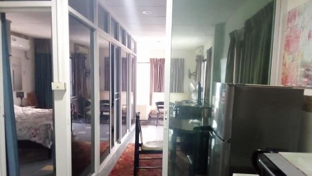 A hotel room with a sliding glass door leading to a balcony, a bed, a desk, and a refrigerator. - Room-big Charming Suite With Balcony in (Pattaya)