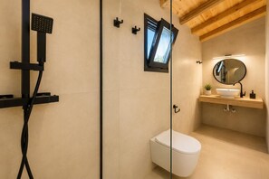Et moderne badeværelse med en glasvæg omkring brusebad, toilet og et toiletbord med spejl og vask.
