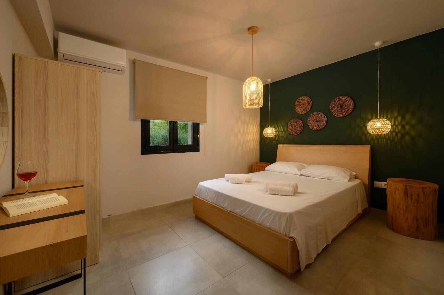 A modern bedroom with a wooden bed, a bedside table with a book and glass, a window with a view, and decorative wall art.