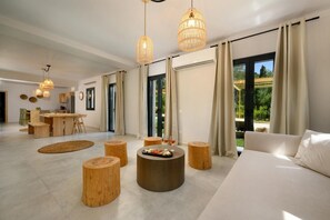 A modern living room with a sofa, round wooden stools, a coffee table, and pendant lights. - Villa Natalia - Four Bedroom Villa, Sleeps 8 (Kato Garouna)